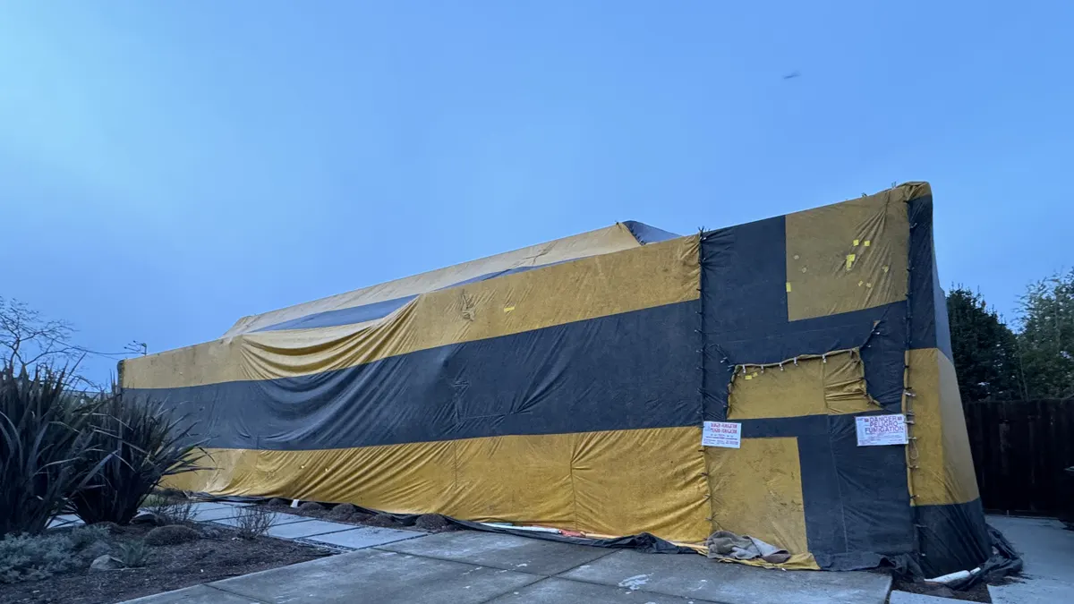 A low building fully wrapped in yellow and black fumigation tarps at dusk