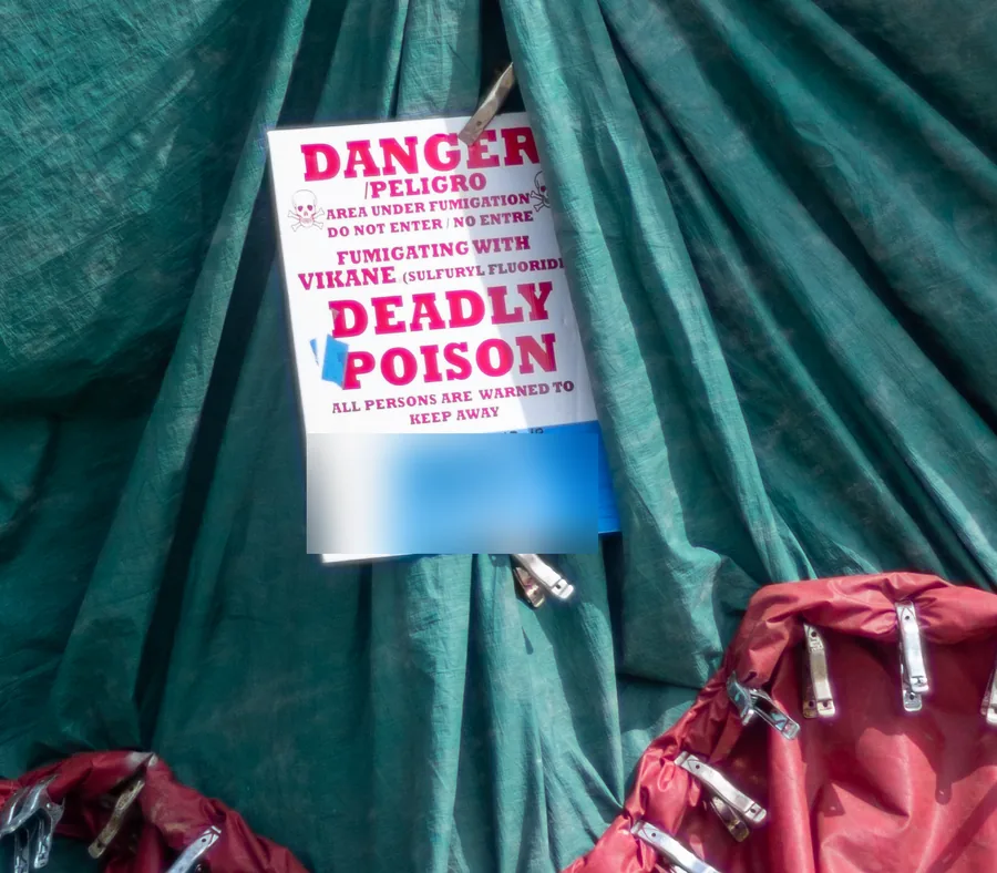 A red and white Danger, Deadly Poison warning sign in English and Spanish, pinned to a green fumigation tarp